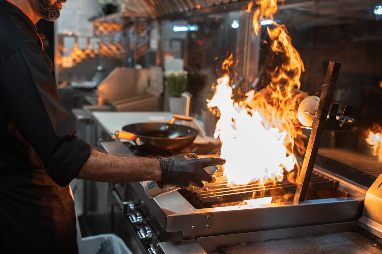 A chef expertly grills meat on an open flame in a professional kitchen setting.