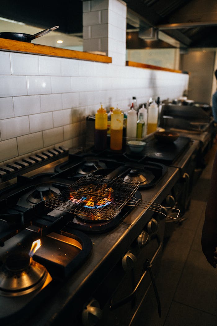 A commercial kitchen featuring a grill with open flames and assorted bottles, highlighting cooking dynamics.